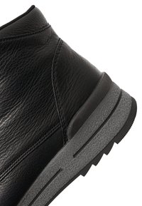 Zwarte leren enkellaars met een gestructureerde grijze zool en gedetailleerd stiksel, getoond in een close-up vanuit een schuine hoek.