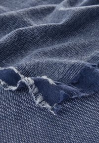 Tissu en denim avec un tissage texturé en bleu foncé, présentant des bords effilochés et des nuances variées pour une profondeur et un détail visuels.