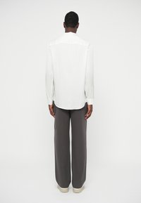 Hvite stripete langermet skjorte med buet kant, kombinert med grå vide bukser og lyse sko.