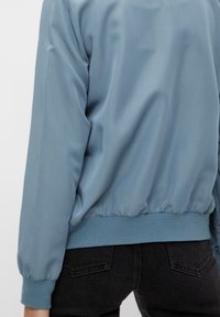 Lys blå satin bomberjakke med en rund kant, elastiske manchetter og talje. Glat tekstur, afslappet design og minimalistisk stil.