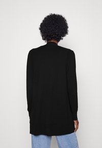 Long gilet noir à coupe décontractée, col arrondi et manches longues. Fabriqué dans un matériau doux, avec une texture lisse.