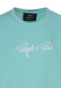 T-shirt en coton turquoise avec un col rond et un texte brodé blanc "Project x Paris" sur le devant. Texture lisse.