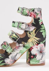 Chaussure noire à talon haut avec talon épais, recouverte d'un tissu fleuri coloré et équipée de quatre brides réglables avec boucles argentées.