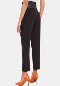 Pantaloni neri, sartoriali, con una cintura alta in finta pelle. Tessuto liscio, design con gambe affusolate, abbinati a tacchi alti arancioni brillanti.