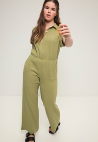 Olivgrüner Overall mit kurzen Ärmeln, Knopfleiste und elastischem Bund. Weite Beinform mit strukturiertem Stoff und seitlichen Taschen.