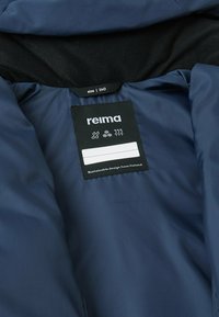 Innenansicht einer navyblauen isolierten Jacke mit glatter Textur. Das Pflegeetikett zeigt die Größe 14.0 und das Nachhaltigkeitslabel von Reima, Finnland.
