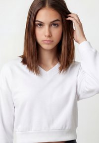 Sudadera blanca recortada hecha de tela suave, con escote en V, puños acanalados y textura lisa. Diseño simple y limpio.