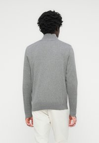 Grauer Strickpullover mit hohem Kragen und geripptem Saum, mit langen Ärmeln und einer weichen Textur, getragen über hellen Hosen.