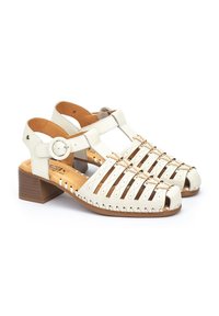 White leather sandals with open toe, multiple striped cutouts, a round buckle strap, and a low wooden block heel.