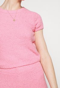 Krótki różowy top o teksturowanej powierzchni z krótkimi rękawami, z okrągłym dekoltem i miękkim, puszystym materiałem. Uzupełniony prostą złotą zawieszką na naszyjniku.