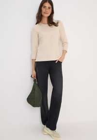 Beige kolmekvart sleevesi särk, mustad sirged teksad ja heledad tossud. Hoides tume roheline, tikitud käekotti. Lihtne, mugav riietus.