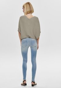 Losse taupe trui met een V-uitsnijding aan de achterkant, gecombineerd met lichtblauwe skinny jeans met een vervaagde verloop, en zwarte sandalen met bandjes.