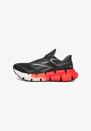 Zapatilla de correr en negro y gris con una parte superior texturizada, que presenta una suela exterior distintiva en rojo y blanco con amortiguación segmentada para mayor soporte.