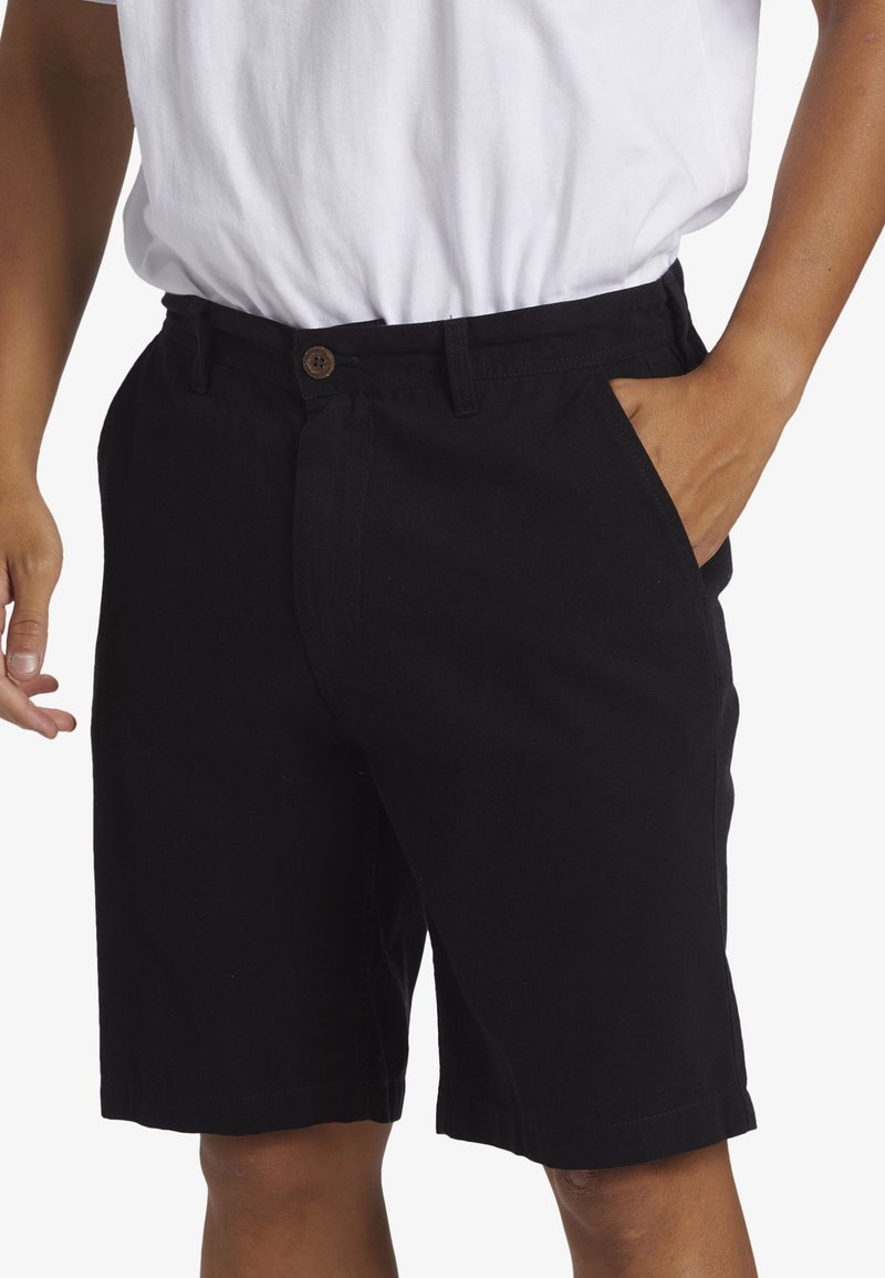 Black cotton shorts with a straight cut, front pockets, and a brown button closure, paired with a white t-shirt.