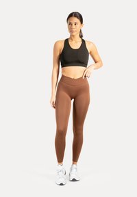 Schwarzer Sport-BH mit schlankem Design und breiten Trägern, kombiniert mit braunen, hoch taillierten Leggings, beide aus glattem, elastischem Stoff.