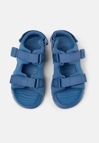 Sineliset sandaalit, joissa on teksturoitu, muotoiltu kumipohja ja säädettävät kangasnauhat, joissa on leikattuja kohtia ja sileä pinta.