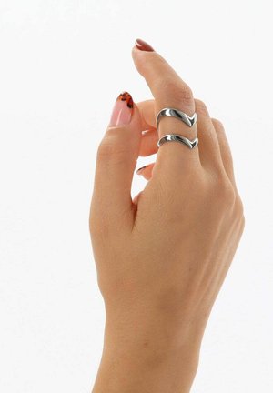 Mano con unghie laccate color nudo e con stampa leopardata che tiene due anelli d'argento con motivi ondulati sul dito medio.