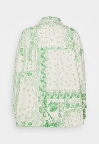 Camicia a maniche lunghe con motivo patchwork floreale e paisley verde su tessuto bianco sporco, vista da dietro.