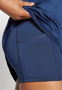 Shorts de sport navy en tissu lisse et extensible, avec une poche latérale et des coutures visibles pour une structure supplémentaire.