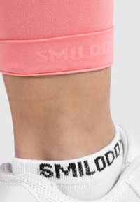 Leggings attivi rosa con una morbida texture e una cintura elasticizzata a contrasto. Calzini alla caviglia bianchi con un logo nero.