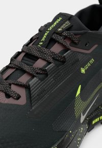 Black sneaker with textured Gore-Tex upper, maroon accents, and reflective details. Features patterned laces and a speckled outsole.