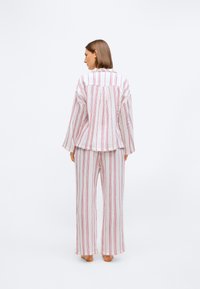 Pasiasty zestaw odzieży domowej w białym i czerwonym kolorze, z luźnym krojem, długimi rękawami i szerokimi spodniami wykonanymi z lekkiego materiału.