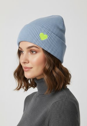 Himmelblaues gestricktes Beanie mit umgeschlagenem Bündchen, das ein kleines grünes herzförmiges Patch an der Seite aufweist. Glatte Textur, weiches Material.