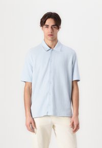Polo de manga corta azul claro, hecho de una tela suave y texturizada, con botones en la parte delantera y un cuello clásico.