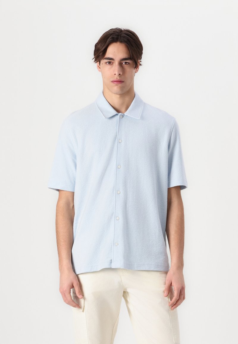 Polo de manga corta azul claro, hecho de una tela suave y texturizada, con botones en la parte delantera y un cuello clásico.