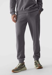 Graue Jogginghosen aus Baumwollmischung mit elastischem Bund und Bundabschlüssen, seitlichen Taschen und einer glatten Textur. Kombiniert mit grünen Sneakers.