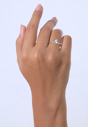 Silberring mit einem Design eines Rentierkopfes und roten Akzenten. Wird an einer Hand mit hellbeiger Nagellack getragen. Glatte Textur und dünner Ring.