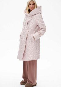 Wypełniona, jasnoróżowa kurtka z geometrycznym pikowanym wzorem, oversizowy kołnierz i boczne kieszenie. Noszona na luźne, dopasowane spodnie.