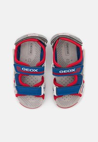 Røde og blå sandaler med mesh-overdel, Velcro-stropper, gummisåler og grå indlægssåler; har Marvel-branding på siderne.