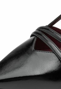 Scarpa in pelle verniciata nera con punta affusolata e design a cinturino incrociato. Presenta un dettaglio a intaglio e foderatura interna color bordeaux.