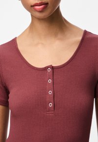 Kortsleeve ribatopp burgundis, millel on ümara kaelusega ja viis avatud nööbi sulgemist esiküljel.