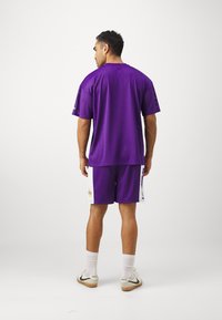 Set di maglia e pantaloncini viola, realizzato in tessuto a rete. Design comodo con maniche corte e accenti bianchi sui pantaloncini.