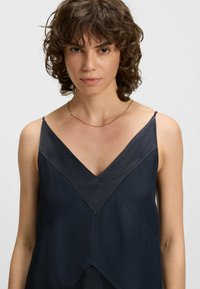 Granatowa bezrękawnik z dekoltem w serek, z warstwowym fasonem i teksturowanym trójkątnym akcentem. Gładki materiał z minimalnymi dodatkami.