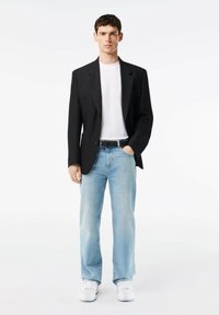 Blazer negro sobre una camiseta blanca, jeans rectos de mezclilla azul claro, cinturón negro y zapatillas blancas. Tejido suave, corte ajustado, estilo casual.