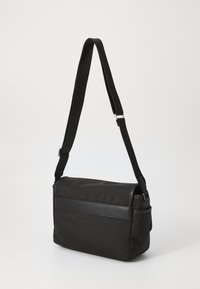 Borsa messenger nera realizzata in tessuto testurizzato con un accento in pelle liscia. Presenta una tracolla regolabile e una chiusura a patta.