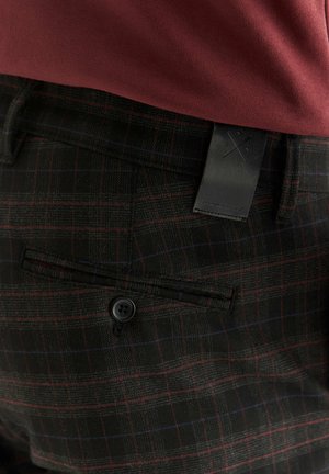 Czarne spodnie w kratę z delikatnym wzorem w czerwonym i niebieskim kolorze, z skórzaną metką i jednym czarnym guzikiem na tylnej kieszeni.