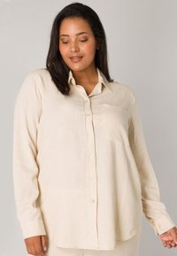 Cream button-up shirt made of a light fabric, featuring long sleeves, a chest pocket, and a relaxed fit with a smooth texture.