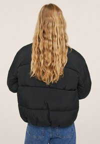 Czarna kurtka puchowa o prostym kształcie i żeberkowym wykończeniu. Gładka tkanina z widocznymi pikowanymi sekcjami. Noszona z niebieskimi dżinsami.