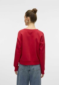 Sweatshirt rouge avec un large col et des épaules tombantes, associé à un jean bleu ample taille haute. Tissu doux avec une texture lisse.