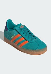 Turquoise suede sneaker with orange stripes, purple heel, and textured rubber sole. Features a padded collar and lace-up front.