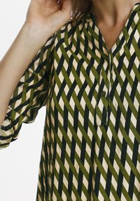 Camicia a maniche lunghe verde e beige con motivo, dotata di scollatura a V, chiusura a bottoni e maniche ampie con un design geometrico a onde.