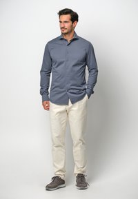 Camicia grigia a maniche lunghe, con bottoni e vestibilità slim, abbinata a pantaloni color crema e scarpe da ginnastica grigie. Tessuto morbido e design classico.