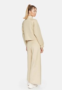 Beige cropped sweatshirt met lange mouwen en een hoge halslijn, gecombineerd met wijde broek in dezelfde kleur. Zachte textuur.