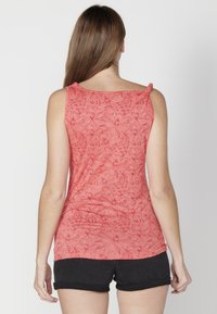 Punane tank top lillemustriga, sileda tekstuuri ja laia kaelusega, millele on lisatud mustad lühikesed püksid, vaadatud tagant.