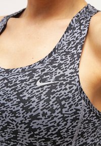 Canotta sportiva grigia con un motivo astratto nero testurizzato. Presenta un scollo rinforzato e un piccolo logo Nike sul petto.