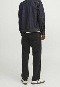 Chaqueta de mezclilla oscura con mangas largas, combinada con pantalones negros holgados y zapatillas blancas. Presenta costuras simples y elementos de diseño clásicos.